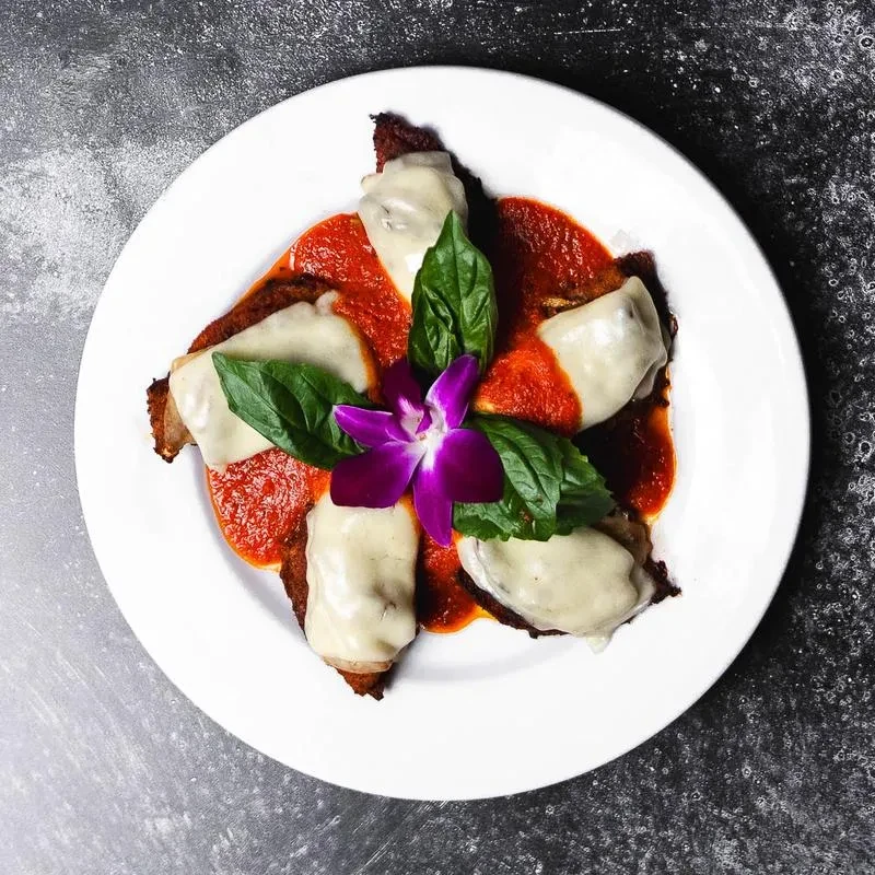 Plated chicken parmesan with basil and purple orchid on dark background.