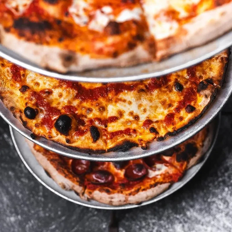 Three stacked pizzas on metal trays, middle one with olives and cheese.