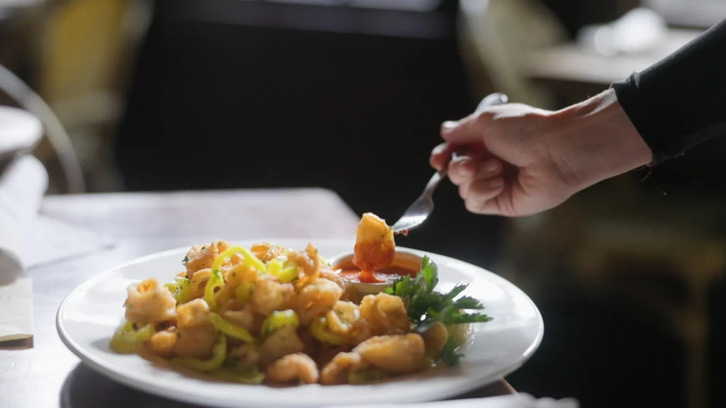 Hand dips fried calamari and banana peppers into marinara sauce.