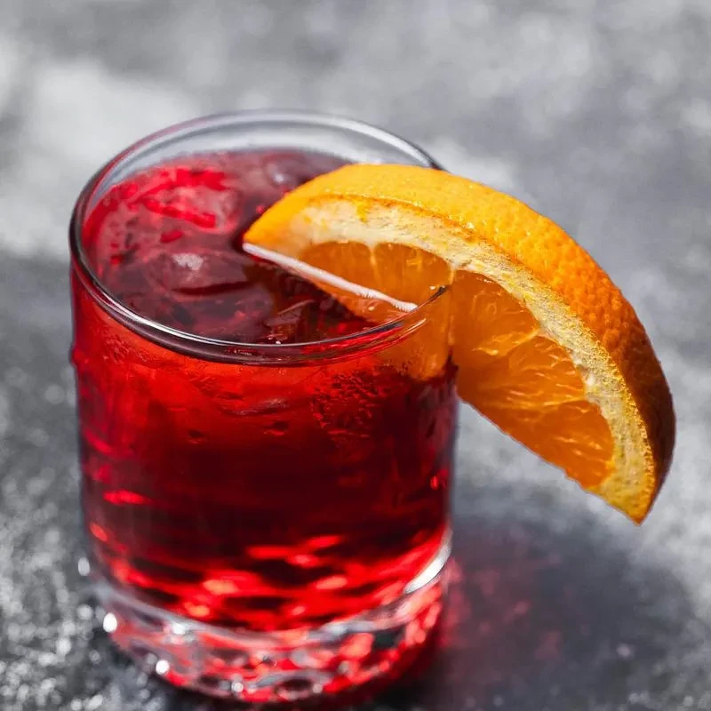 Chilled red cocktail in faceted glass, garnished with orange slice.