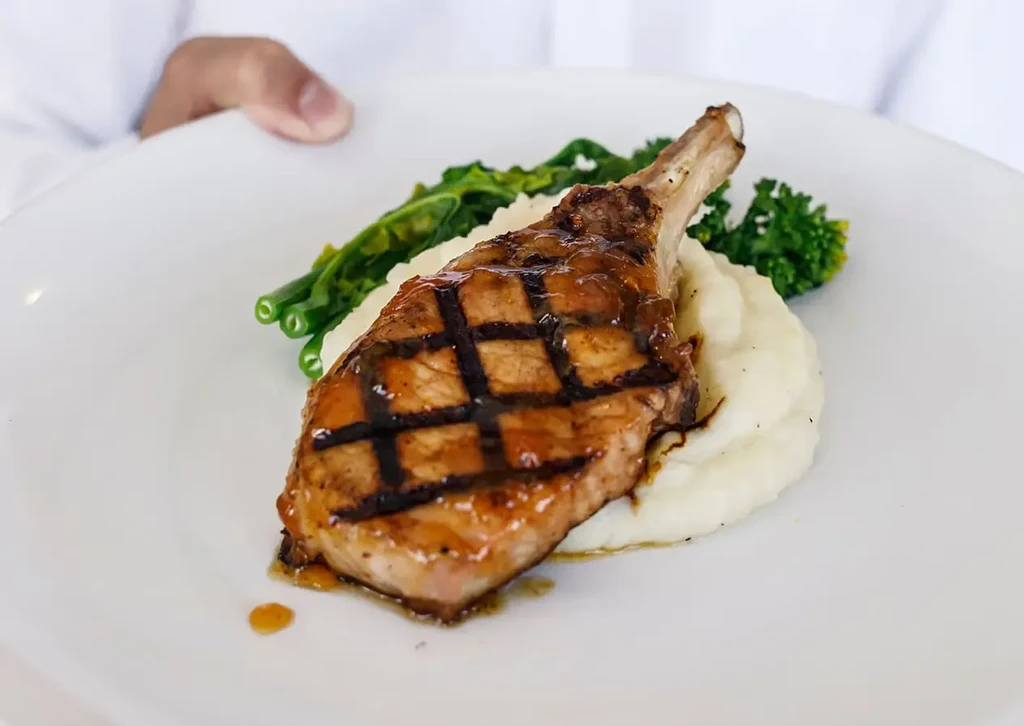 Grilled bone-in chop, mashed potatoes, and green vegetables served.
