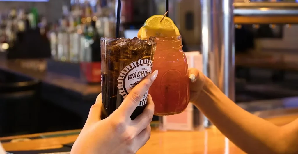 Two hands clinking drinks, one with a Wachus Brew Co. logo.