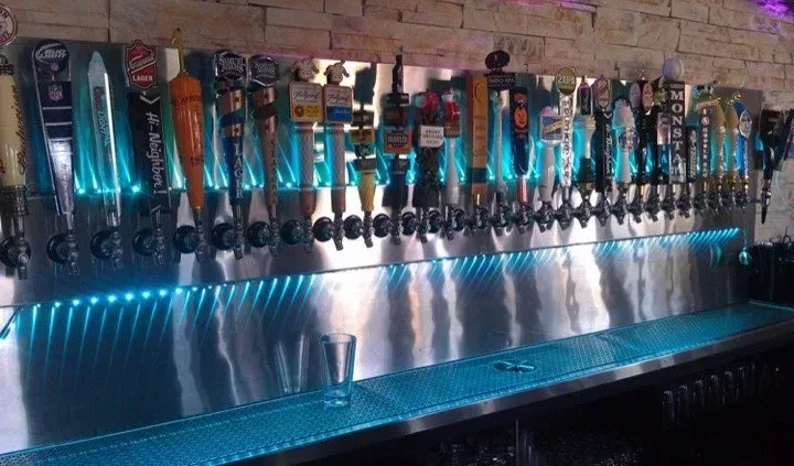 Numerous beer taps on a blue-lit stainless steel wall.