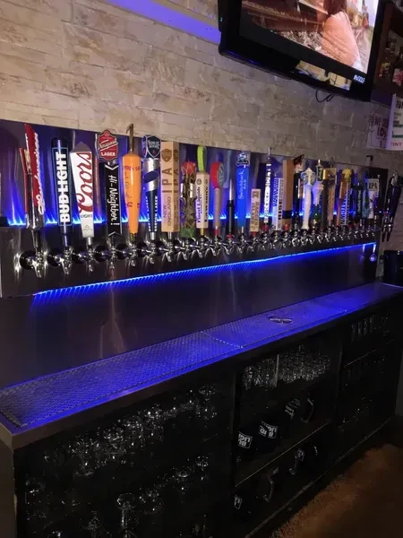 Numerous chrome beer taps line a blue-lit brick bar wall.
