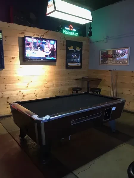 Black felt pool table in a dimly lit bar interior.