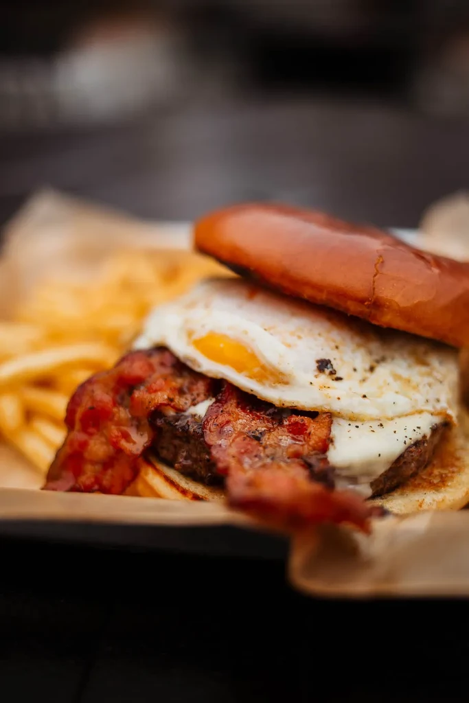 Gourmet burger with bacon, runny egg, melted cheese, and fries.