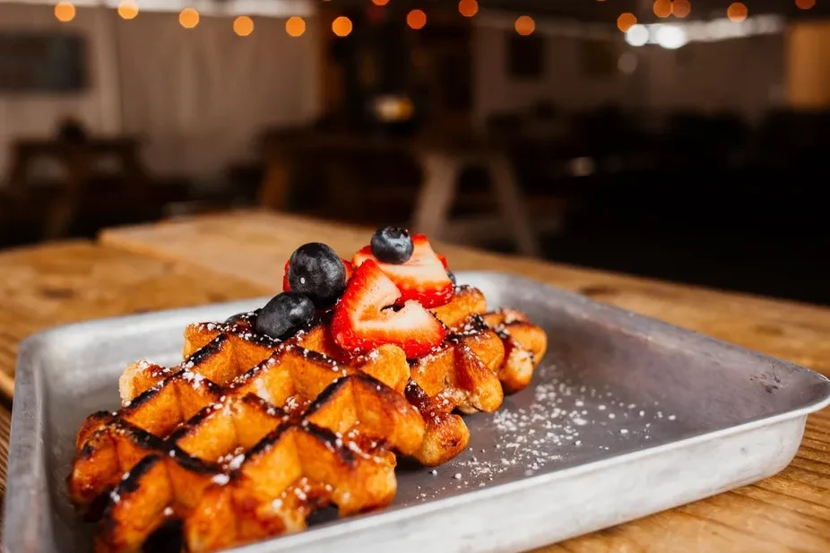 Two golden-brown waffles with strawberries, blueberries, powdered sugar on a tray.