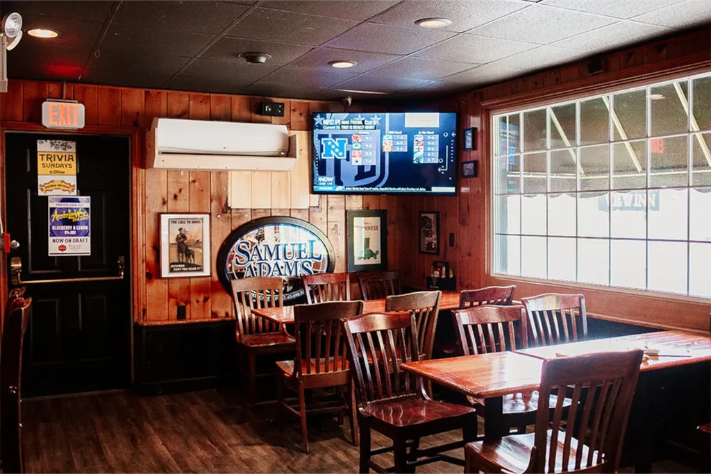 Empty bar interior, wooden tables, Samuel Adams sign, TV shows sports.