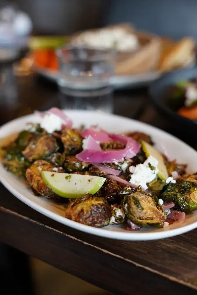 Roasted brussels sprouts with crumbled cheese, red onion, and green apple slices.