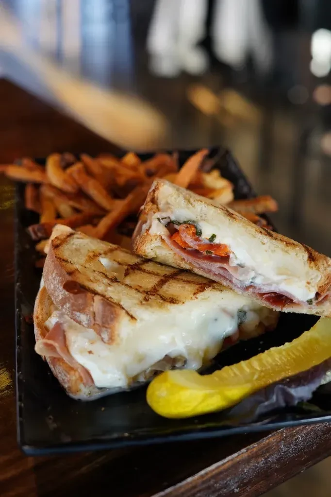 Grilled sandwich with melted cheese, fries, and a pickle spear.