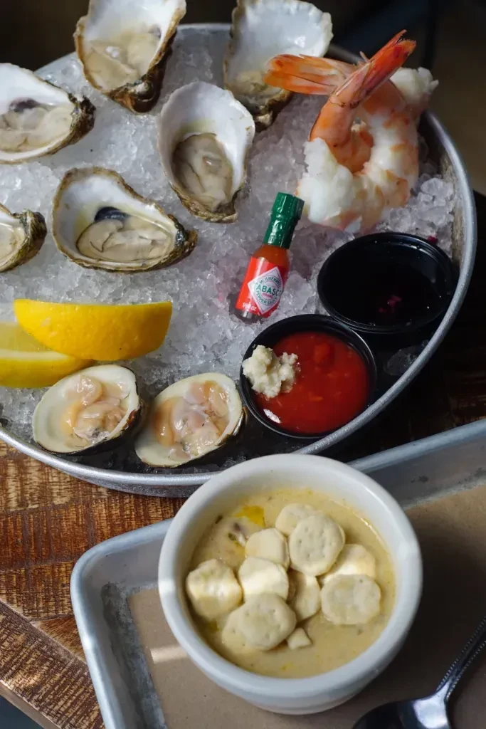 Close-up of oysters, shrimp, clams on ice, with a bowl of chowder.