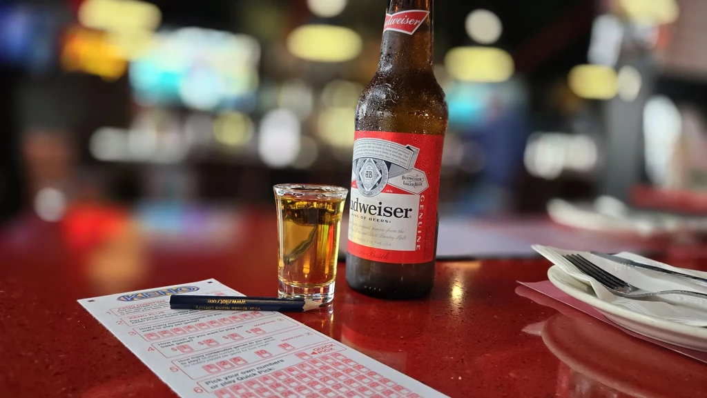 Frosty beer bottle, shot glass, KENO ticket, pencil on red bar.