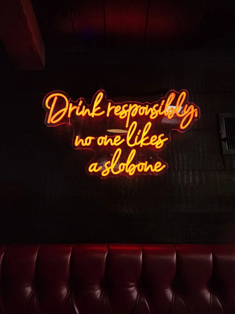 Orange neon sign reads 'Drink responsibly, no one likes a slobone'.