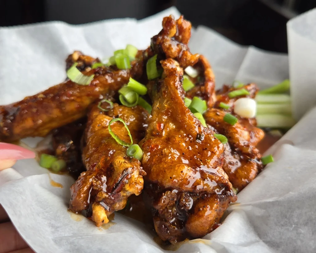 Saucy chicken wings with green onions served in a basket with celery.