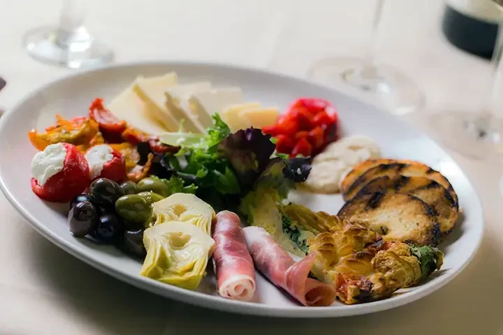 Platter of antipasto with cheese, olives, prosciutto, peppers, artichokes, and crostini.