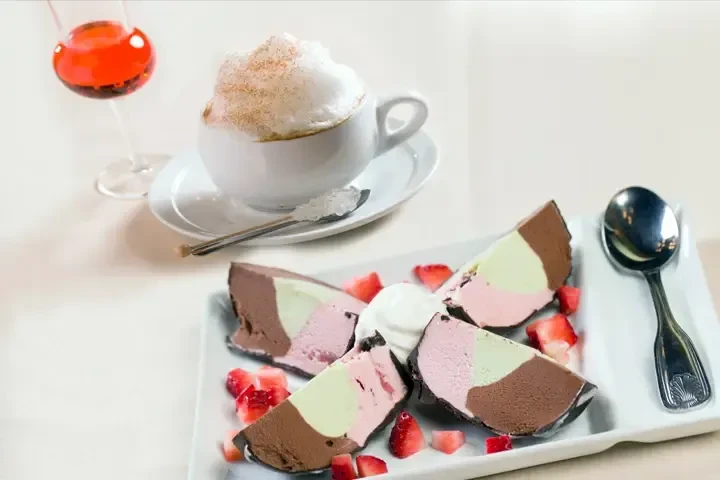 Multi-layered ice cream cake with strawberries, cream, and two beverages.