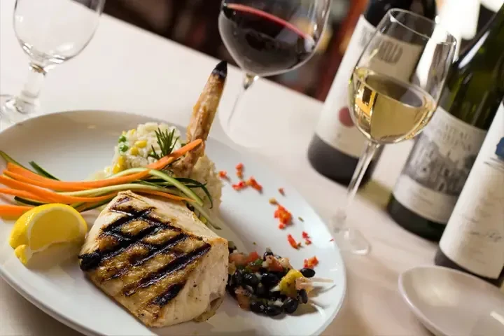 Plated grilled fish/chicken meal with rice, vegetables, salsa, and wine.