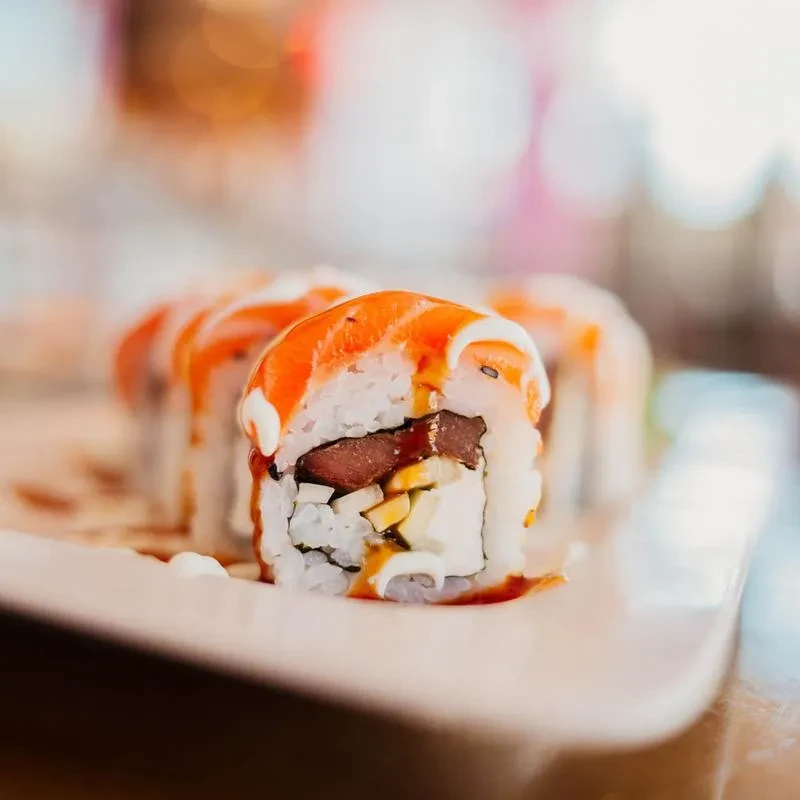 Sushi roll with salmon, tuna, cream cheese, drizzled with two sauces.