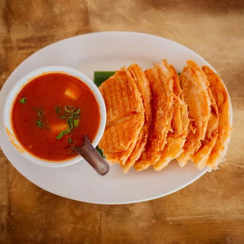 Oval plate with reddish soup and crispy golden food on wood.