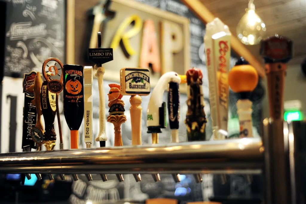 Row of diverse beer tap handles on a metallic bar system.