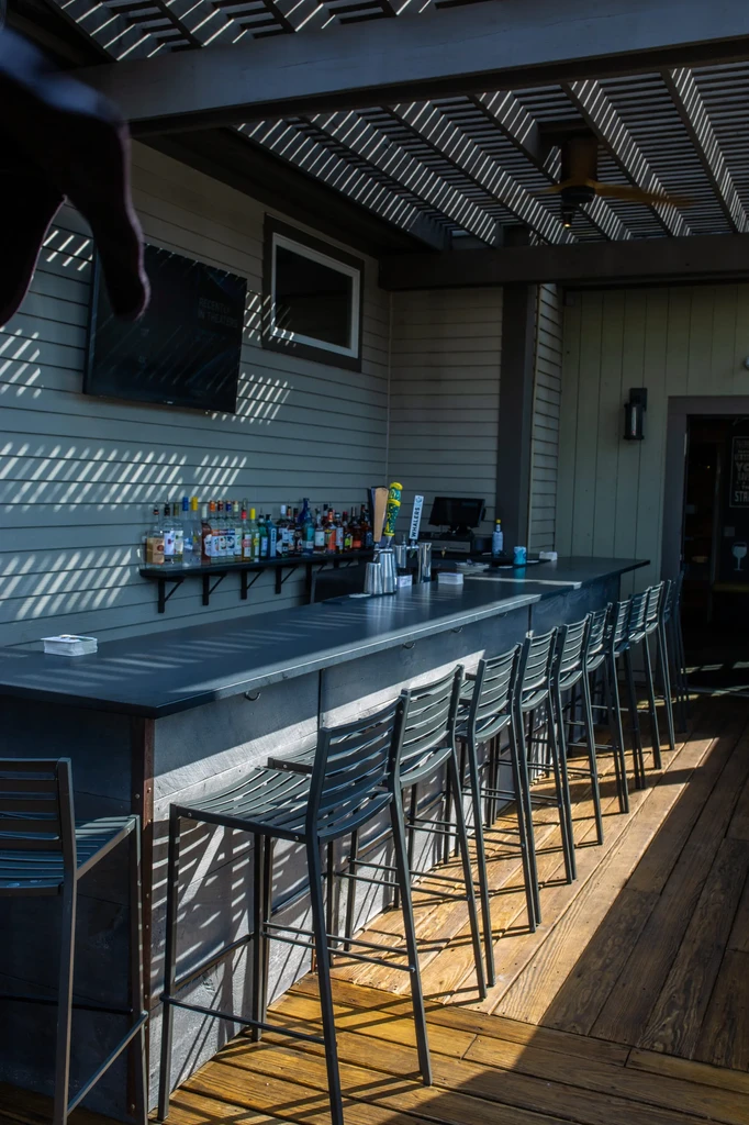 Bright outdoor bar counter with metal stools and liquor bottles.
