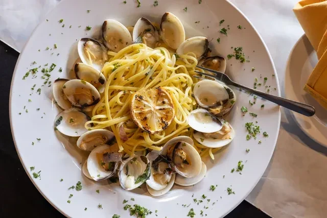 Close-up of linguine with clams, grilled lemon, and a fork.