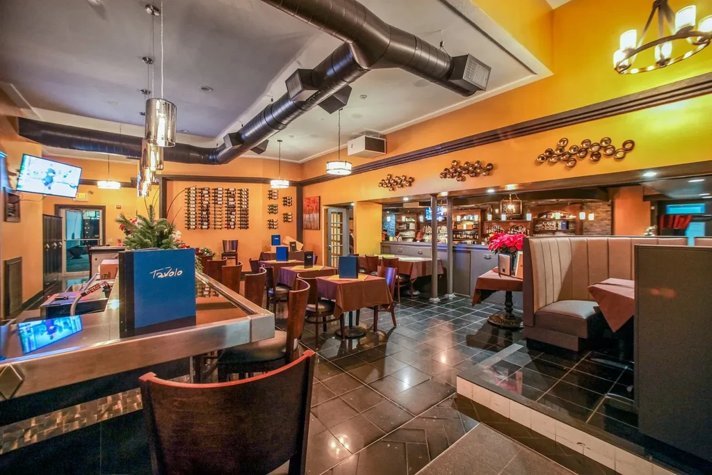 Restaurant interior with orange walls, bar, mixed seating, and TV.