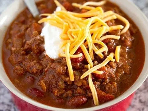 Bowl of chili topped with sour cream and cheddar cheese.