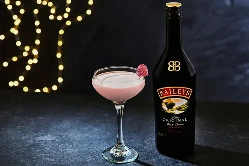 Pink creamy cocktail with raspberry and Baileys Irish Cream bottle.
