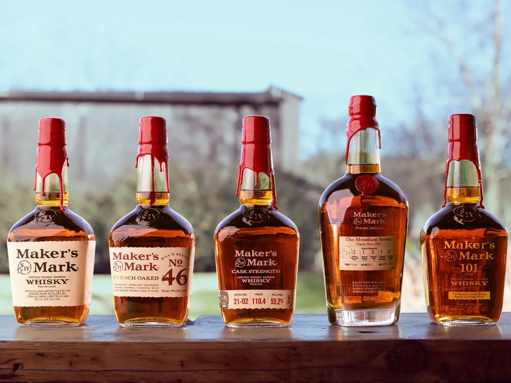 Five distinct Maker's Mark bourbon bottles on a wooden surface.