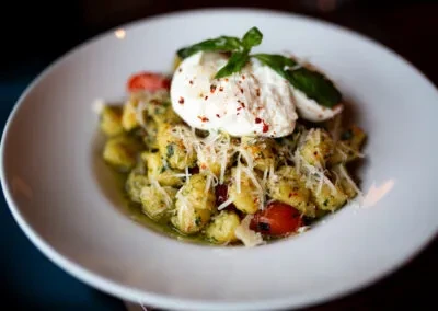 Gnocchi in pesto with tomatoes, topped with cheeses and basil.