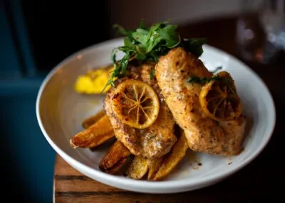 Golden chicken or fish, lemon, potato wedges, and herbs in a bowl.