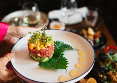 Person's hands hold a layered tartare with red, green, yellow, microgreens.