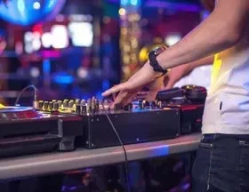 DJ's hands adjust mixer and turntable in a dimly lit nightclub.