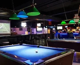 Dimly lit sports bar interior with pool tables and sports on screens.