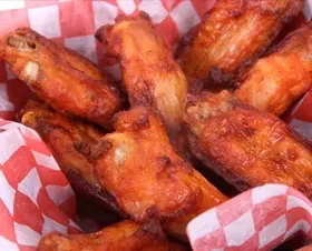 Several golden-brown, crispy fried chicken wings in a checkered basket.