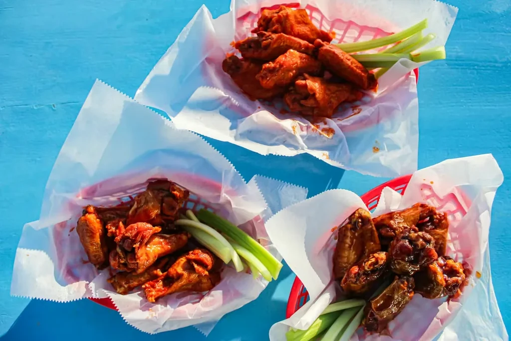 Three red baskets of buffalo and dark glazed chicken wings with celery.