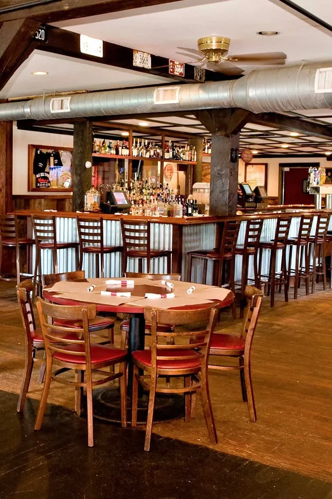 Rustic restaurant interior with dining table, chairs, and stocked bar.