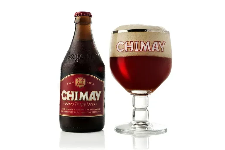 Cold Chimay beer bottle and chalice glass with dark foamy beer.