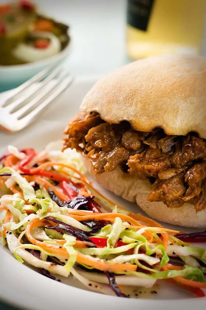 Close-up of shredded meat sandwich, colorful coleslaw on white plate.