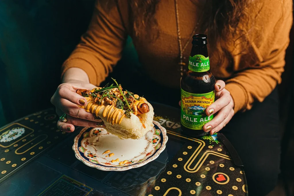 Hands holding a gourmet hot dog and Sierra Nevada Pale Ale beer.