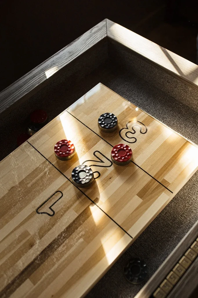 Shuffleboard table with red and black pucks on scoring zones.
