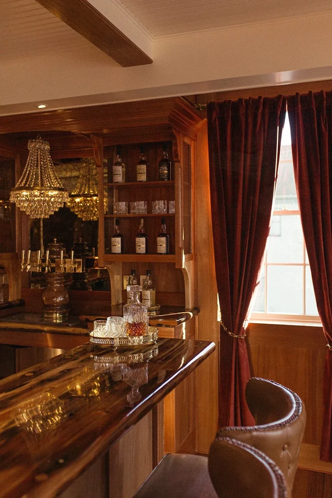 Polished wooden bar counter, crystal decanter, bottles, and chandelier.