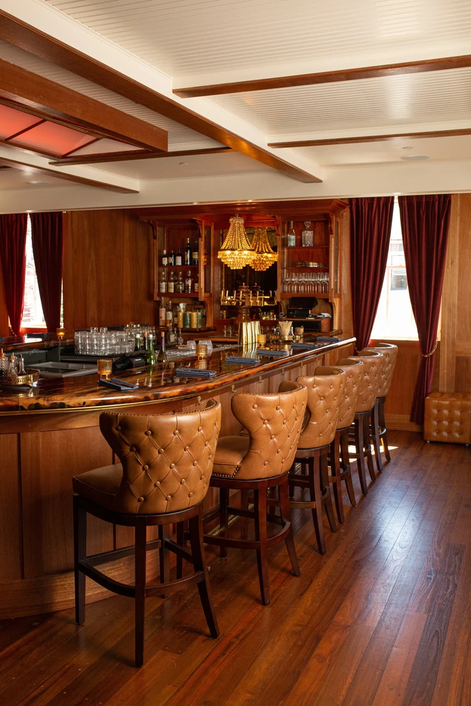 Stocked dark wood bar, six light brown tufted leather stools.