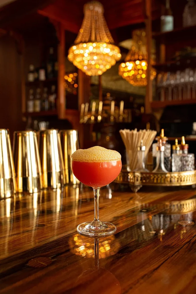 Red cocktail with frothy golden foam on a polished bar.