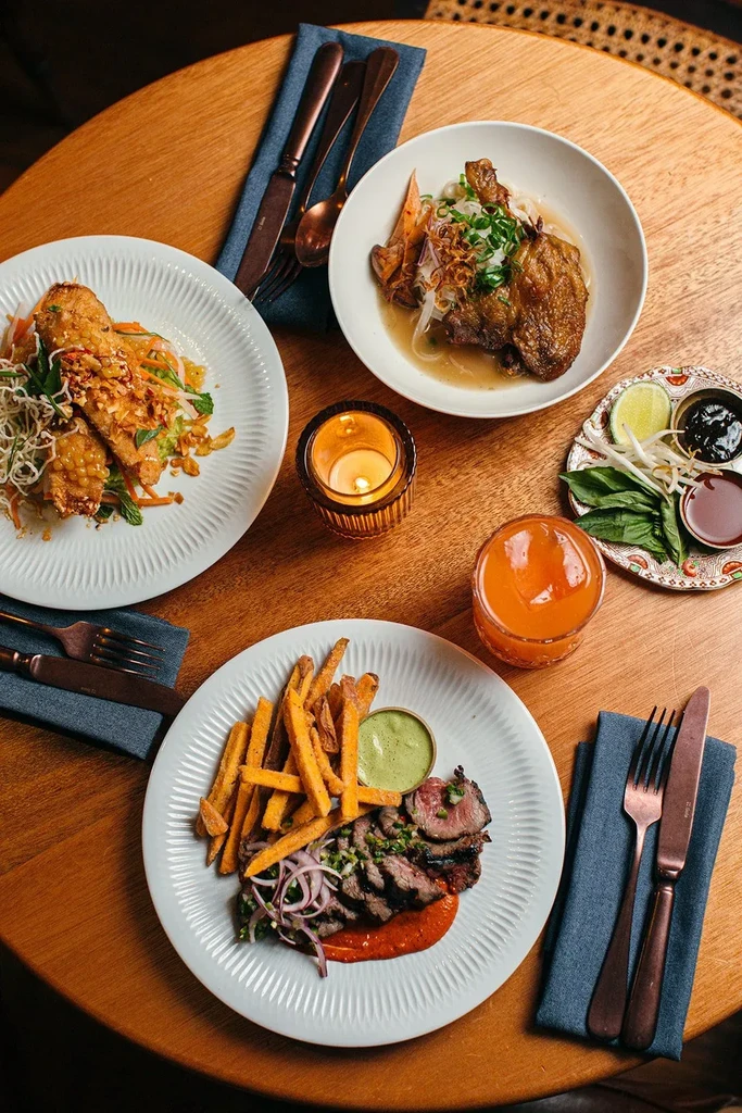 Overhead shot of wooden table with plated food, a drink, and lit candle.