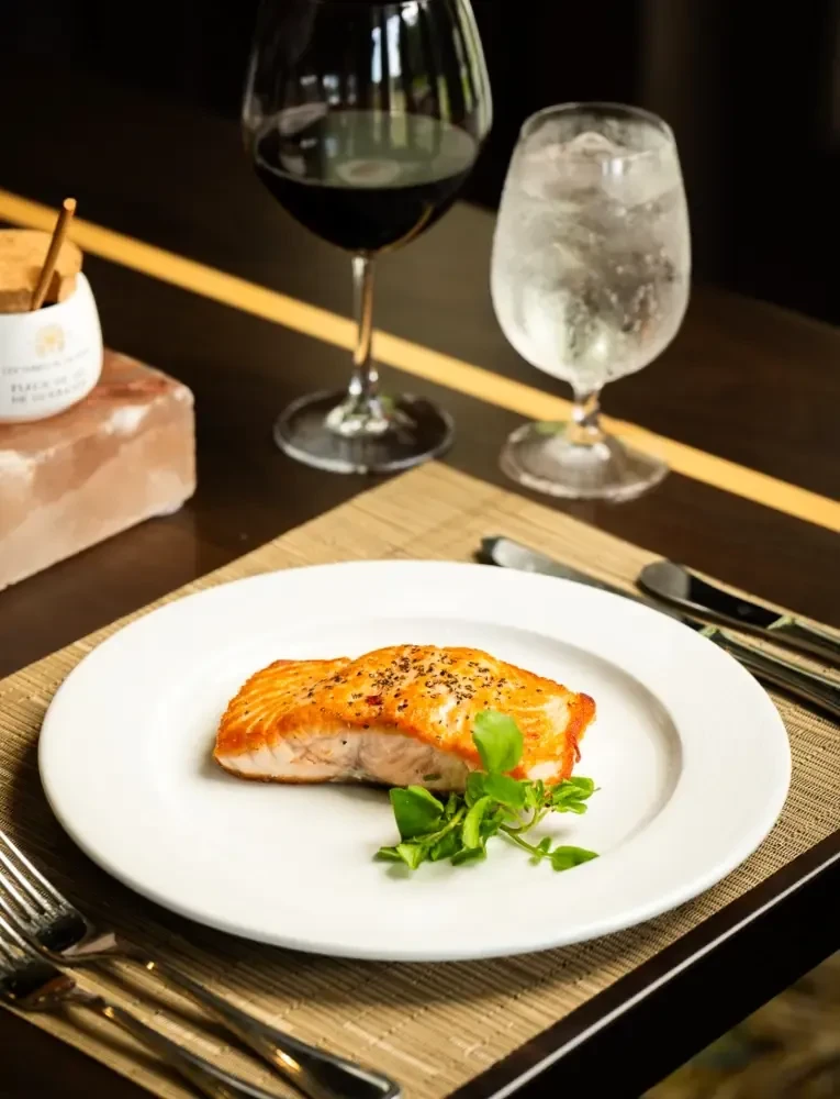 Grilled salmon with greens, cutlery, and drinks on a restaurant dining table.