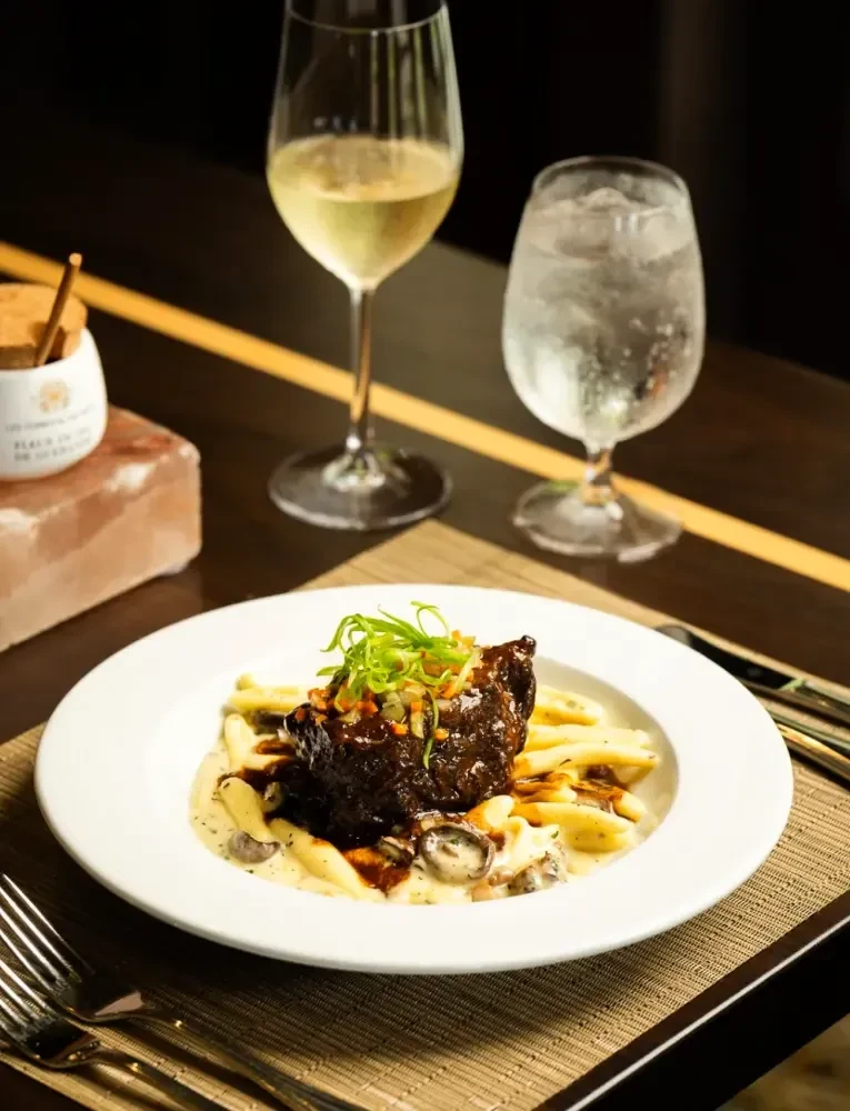 Plated meat and pasta dish with wine, water, and salt cellar.