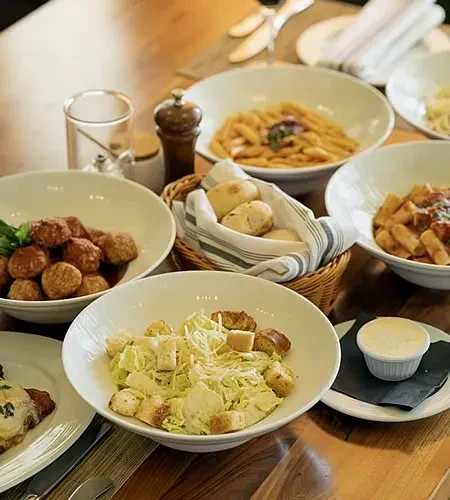 Pasta, meatballs, Caesar salad, and bread rolls on a table.