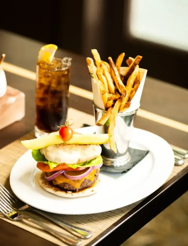 Gourmet burger, fries, and beverage with pickle and tomato.